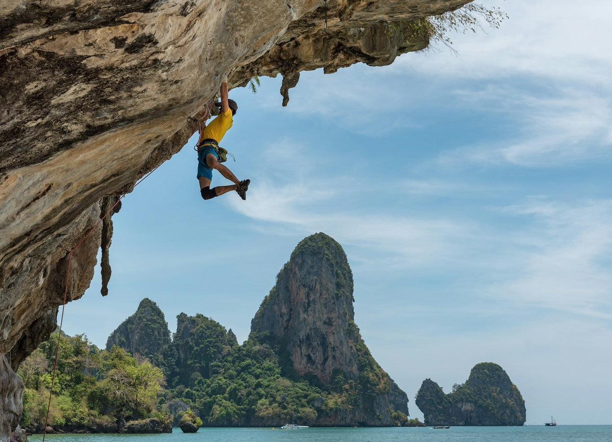 rock climber holding himself in the rock wall only with his grip strength in a tropical landscape