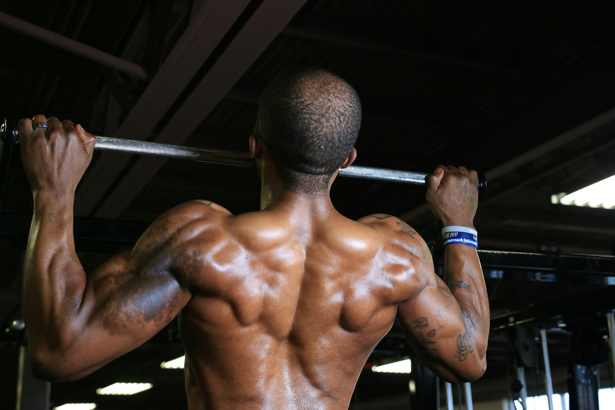 athlete mid pull up with a false grip in a straight bar on a indoor gym view from his back with toned muscles